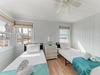 Your peaceful twin bedroom offers stunning sea views through large windows, with coastal breezes from the ceiling fan.