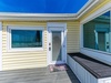 Bright yellow beach house entrance with white trim and wraparound deck, featuring welcome mat and large windows with blinds.