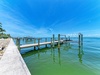 Waterfront property features private boat docks extending into calm turquoise waters, with palm trees lining the sandy shore under endless blue skies.