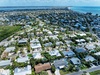 Aerial view of a tropical coastal community with residential homes, lush palm trees, and pristine turquoise waters nearby.