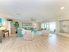 Step into your bright, breezy living space with turquoise accents and coastal charm. Relax in plush seating, feel the ceiling fan's gentle breeze, and gaze through large windows at the inviting pool beyond.