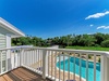 A private balcony overlooks the sparkling pool and lush surrounding greenery, perfect for morning coffee or evening relaxation under clear blue skies.