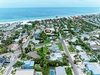 Aerial view of a beachside neighborhood with the highlighted property nestled among palm trees and residential homes, just steps from pristine white sand and turquoise Gulf waters.