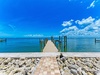 A private dock extends over calm turquoise waters beneath a vivid blue sky dotted with fluffy white clouds, perfect for morning walks and fishing.