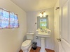 A cozy bathroom featuring a pedestal sink with rolled towels and beach-themed touches. Fresh and ready for your stay, with charming curtains and thoughtful details throughout.