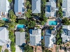 Aerial view of a tropical residential neighborhood featuring multiple private pools, lush palm trees, and well-maintained properties with modern rooflines.
