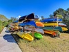 Colorful kayak and canoe rental facility with multiple watercraft options stored on wooden racks in a scenic outdoor setting.