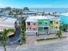 Aerial view of colorful beachside townhomes in a tropical coastal neighborhood, with palm trees lining the streets and pristine ocean waters just steps away.
