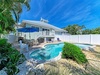 Coastal vacation home with private pool, patio seating, and lush tropical landscaping under sunny Florida skies—your serene retreat awaits.