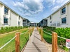 A wooden boardwalk leads through landscaped grounds to modern vacation rental buildings with balconies and coastal charm.