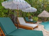 Your private poolside retreat awaits beneath tropical palms, with plush sun loungers, shaded umbrellas, and a thatched-roof cabana creating the perfect spot to unwind in paradise.