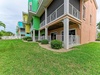 Vibrant Caribbean-style buildings with private balconies surround manicured green lawns and tropical palm trees, creating a colorful and inviting vacation retreat near the beach.
