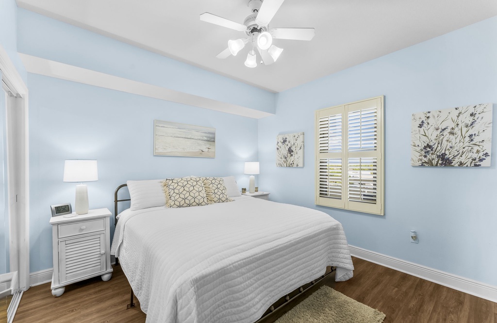 Relax in this serene bedroom featuring soft blue walls and natural light from shuttered windows.