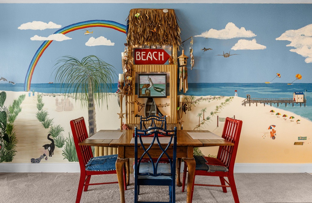 Cozy dining area with a beach-themed mural and colorful chairs.