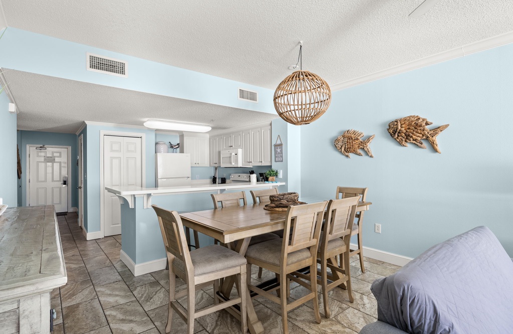 Dining area with wooden table and coastal decor adjacent to a light blue kitchen.