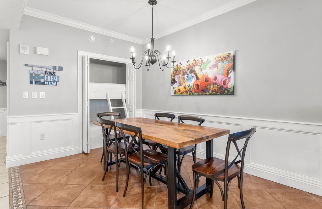 Dining area with a wooden table, six chairs, and a colorful floral painting on the wall