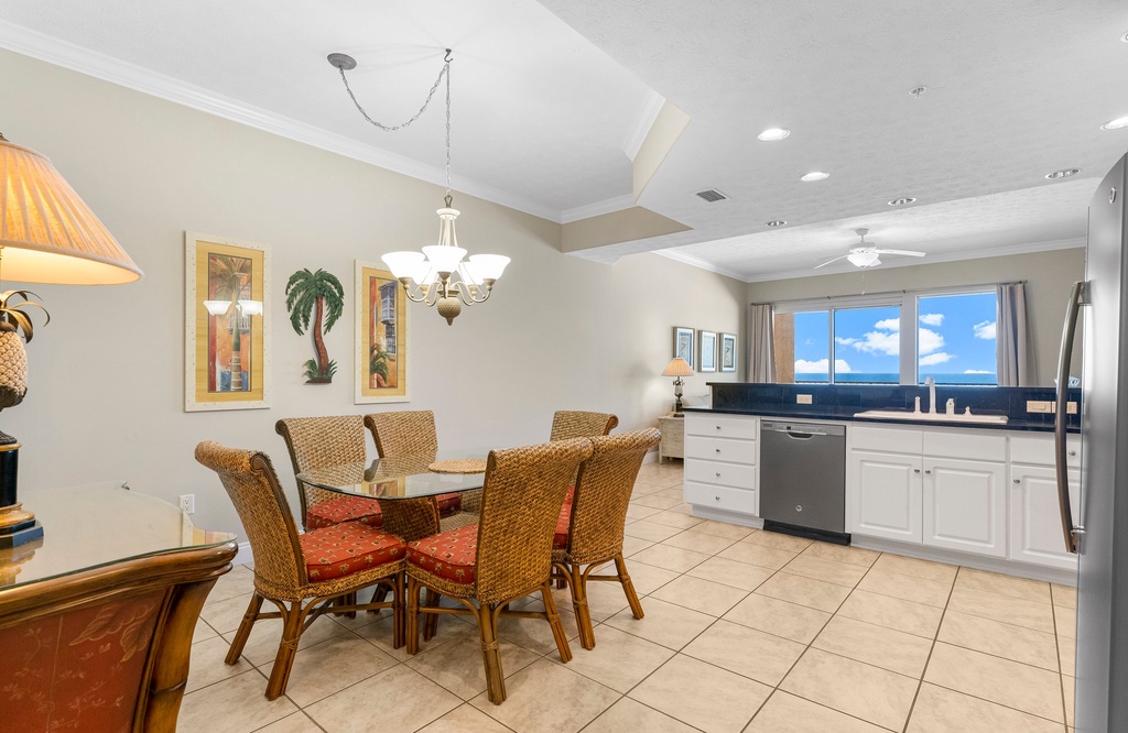 Dining area with wicker chairs and a view of the kitchen and large window.
