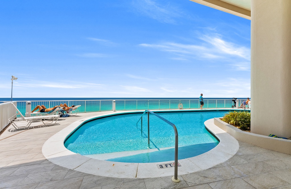 Sparkling beachfront pool overlooking turquoise waters and endless blue skies—your perfect spot to unwind under the Florida sun, just steps from the sand.
