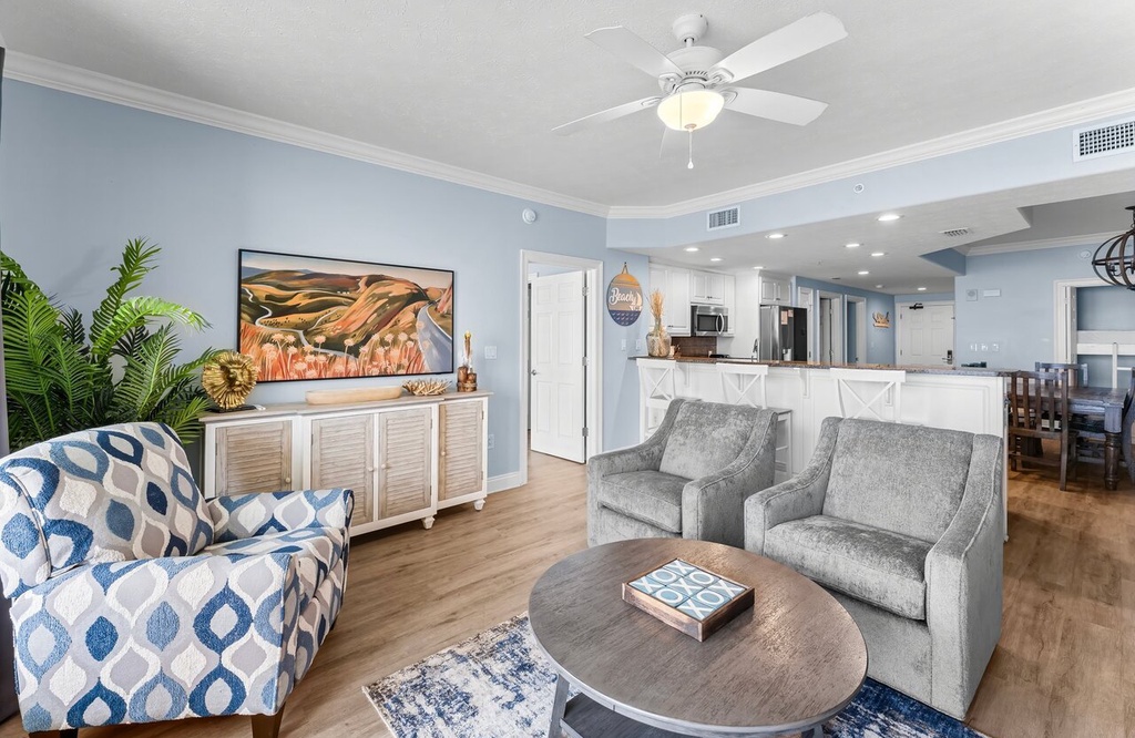 Relax in your open-concept living area featuring calming coastal decor, a plush loveseat, and a fully equipped kitchen—perfect for unwinding after beach adventures.