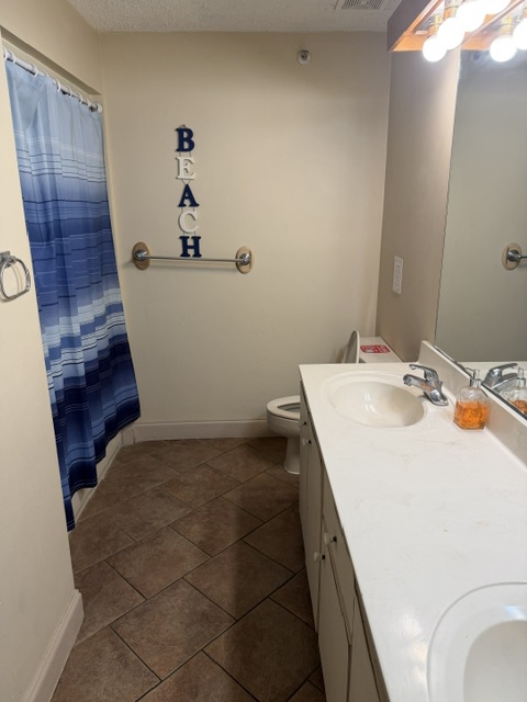 Step into your bright, beach-themed bathroom featuring a clean vanity, tiled floors, and plenty of space to unwind after a day of exploring. The blue gradient shower curtain adds a coastal touch to your morning routine.