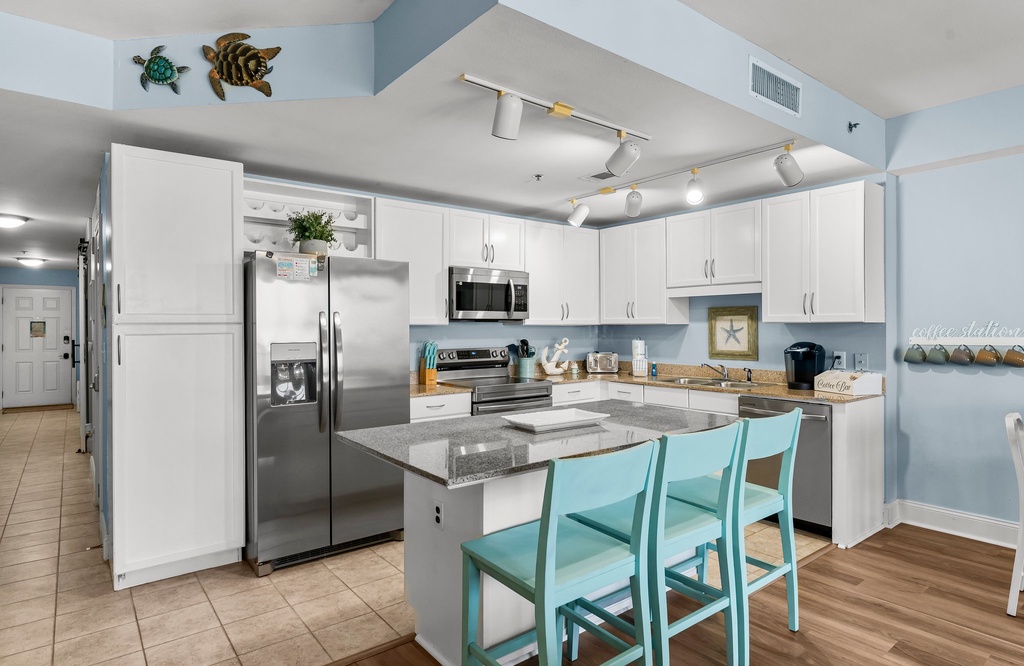 Modern kitchen with stainless steel appliances and a breakfast bar with turquoise chairs.