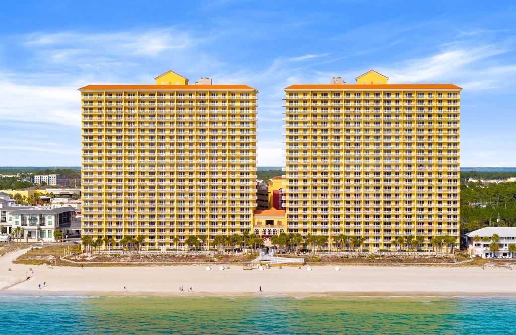 Two high-rise beachfront towers offering direct access to white sand and turquoise waters, framed by coastal surroundings under a clear blue sky.