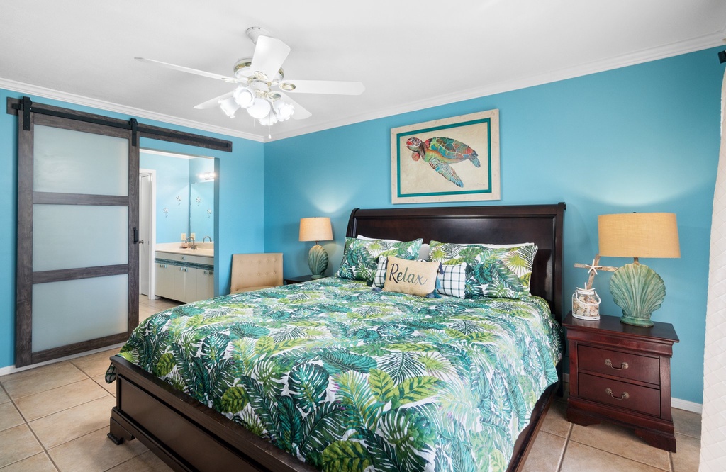 Relax in this tropical-themed bedroom with calming blue walls and natural light.