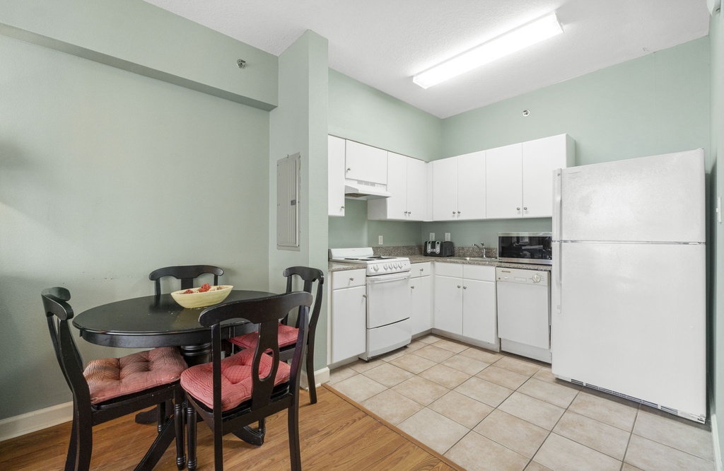 Compact kitchen with white cabinetry and a dining area featuring cushioned chairs.