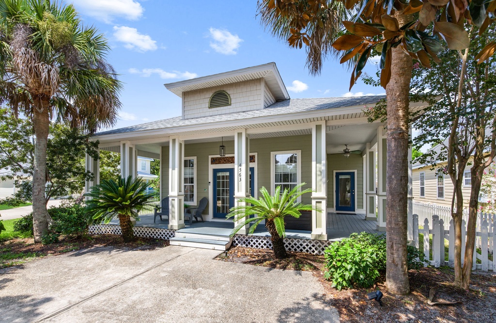 A charming coastal retreat welcomes guests with a spacious front porch and lush tropical landscaping, framed by towering palms and mature trees—perfect for a relaxing getaway.