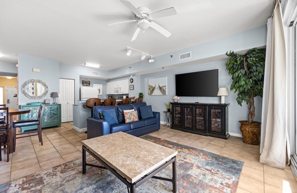 Relax in your bright, welcoming living space with plush seating, ceiling fan, and large TV. Sunlight fills the open layout—perfect for unwinding after exploring nearby beaches.