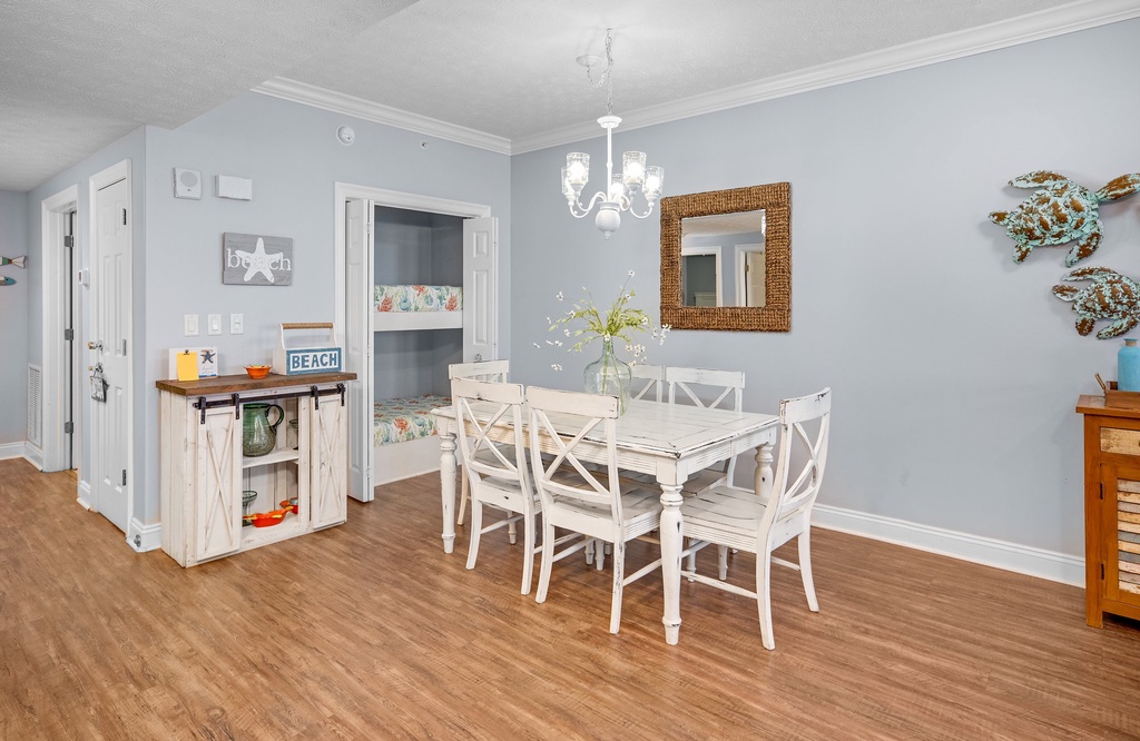 Dining area with a rustic white table and six chairs under a chandelier