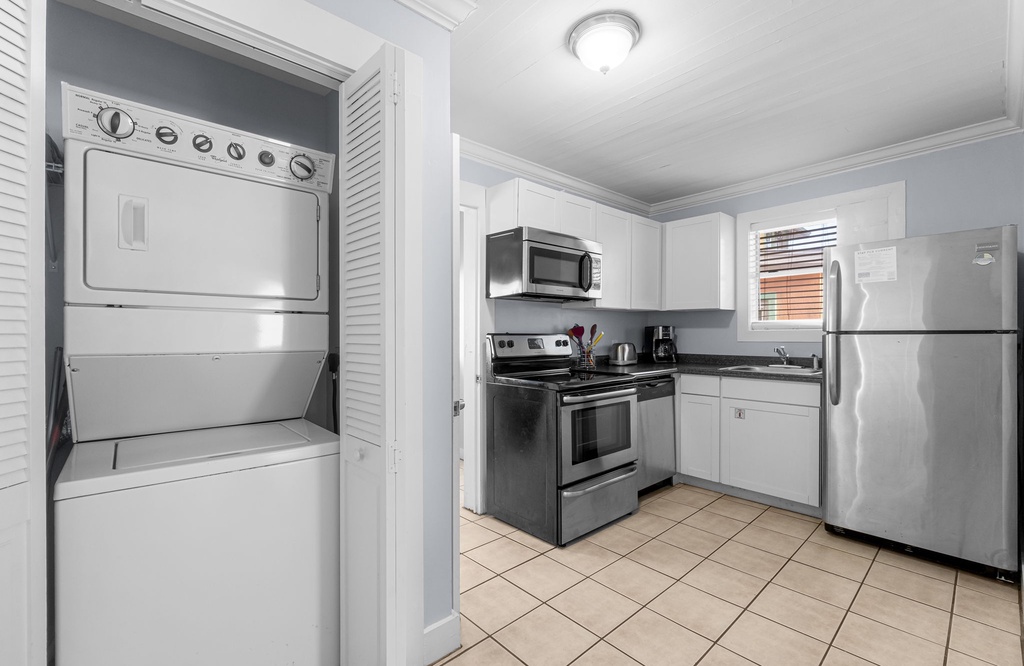 Compact kitchen with stainless steel appliances and a stacked washer and dryer.