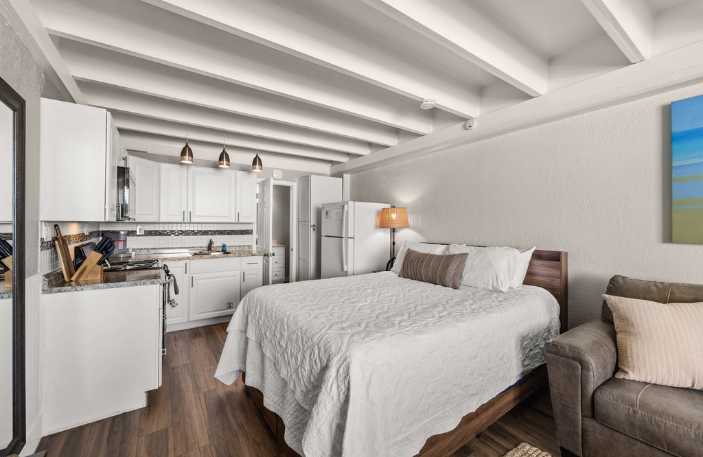 Your open-concept retreat blends comfort and convenience with a plush bed, cozy living area, and fully equipped kitchen—all under striking white beamed ceilings that add character and charm.