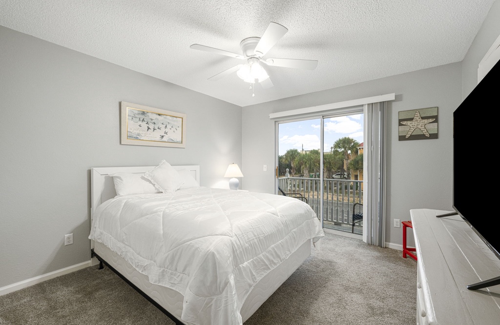 Bright bedroom with sliding glass doors leading to a balcony and a ceiling fan for comfort.