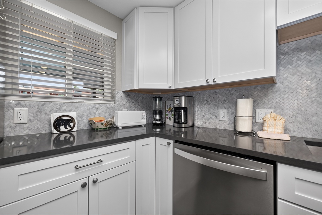 Your bright, modern kitchen features sleek white cabinets, stylish herringbone backsplash, and spacious counters for preparing meals. Coffee maker ready for your morning brew, with storage for all your travel essentials.