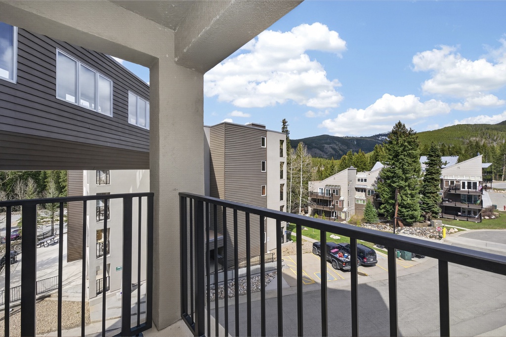 A covered balcony frames a stunning mountain view, overlooking nearby buildings and evergreen-lined peaks—your peaceful retreat amidst nature.