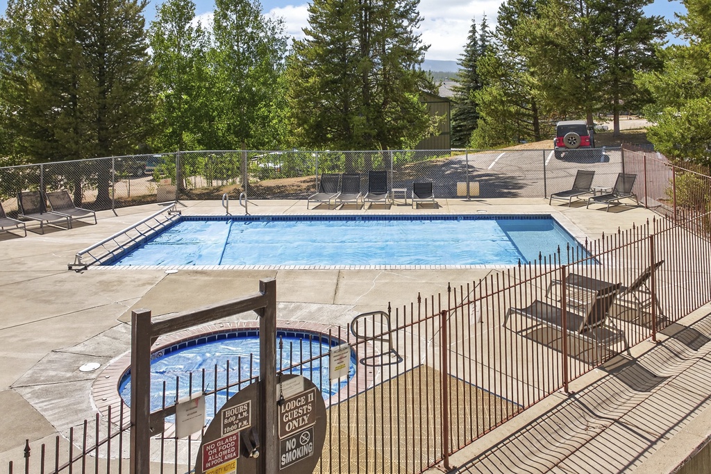 A sun-drenched pool area surrounded by mature pines and mountain scenery, with lounge chairs ready for relaxing afternoons and a hot tub for starlit soaks.