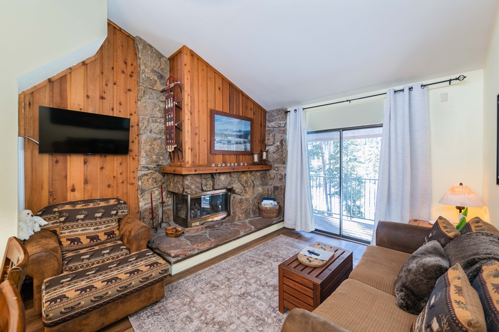 Cozy up by your stone fireplace while enjoying mountain views from the balcony in this rustic living room.