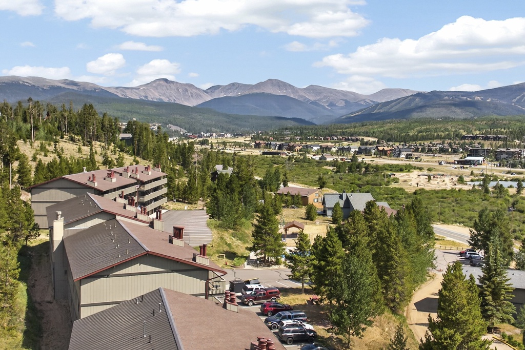 An alpine mountain community nestled among evergreen forests, with dramatic peaks rising beyond the town's residential neighborhoods and tree-lined streets.