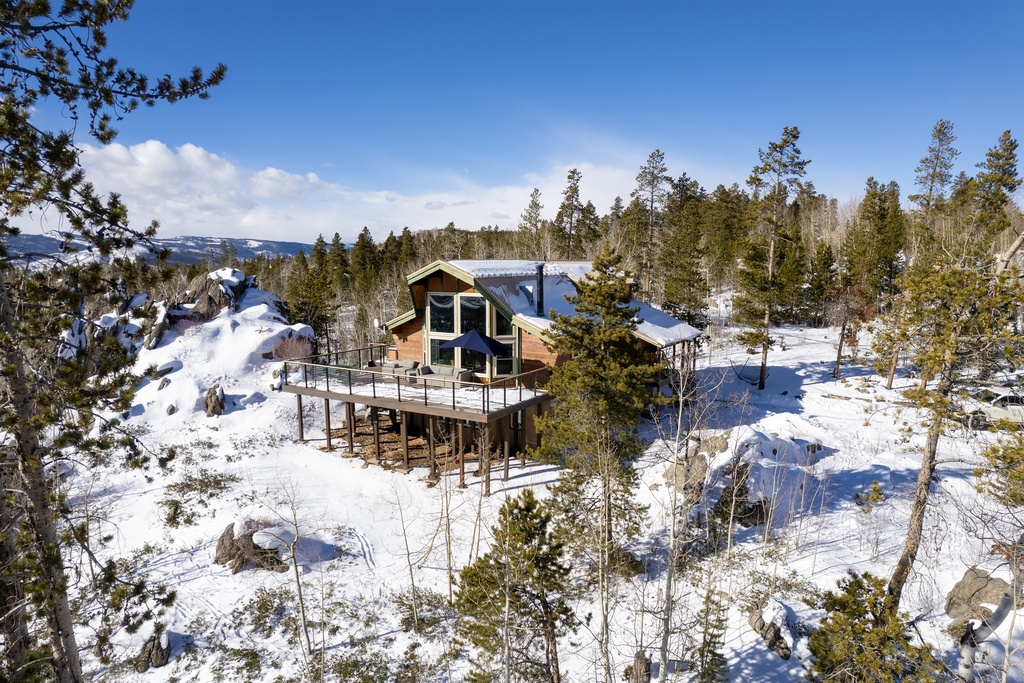 Modern mountain retreat nestled in pristine winter forest with panoramic wilderness views.