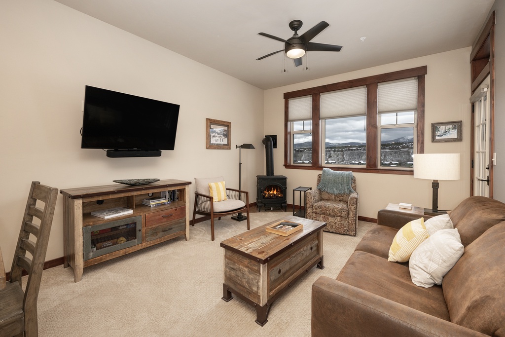 Cozy up in your rustic living room with leather seating, crackling fireplace, and mountain views through charming wood-framed windows.