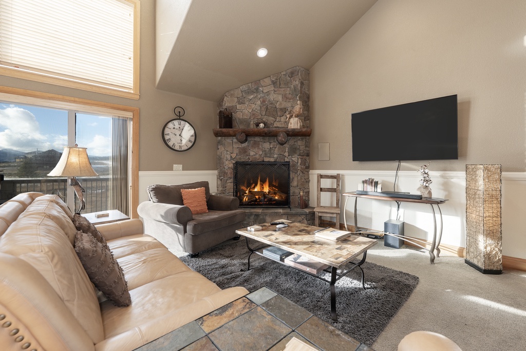 Cozy up in this elegant living room featuring a crackling stone fireplace and stunning mountain views through floor-to-ceiling windows.