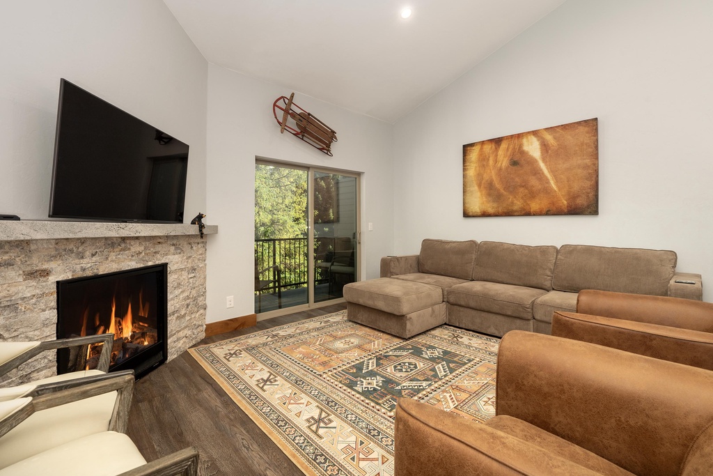 Unwind in your cozy living room with crackling fireplace, plush sectional seating, and mountain views through glass doors.