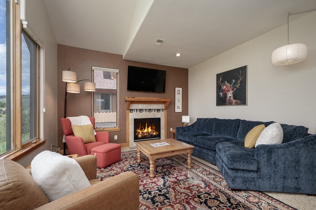 Unwind in your cozy living room where a crackling fireplace meets mountain views through oversized windows, creating perfect moments for relaxation.