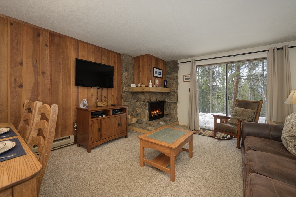 Unwind by your crackling fireplace with mountain views streaming through large windows in this cozy wood-paneled living room.
