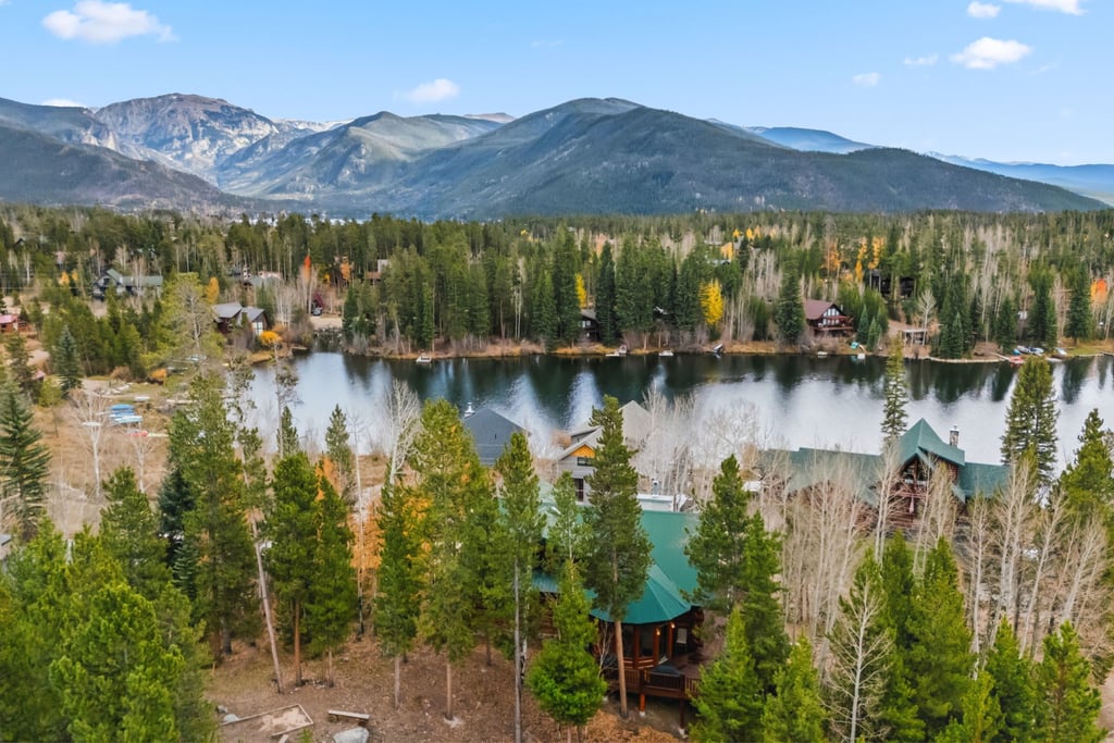 Stunning mountain lakeside property nestled among autumn aspens and evergreens with dramatic Rocky Mountain backdrop.