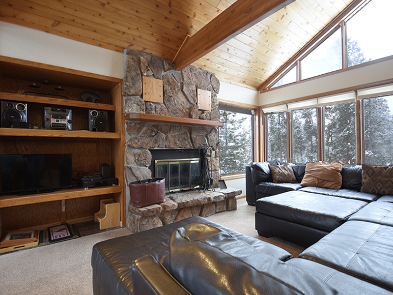 Unwind in your cozy living room with plush leather seating and a stone fireplace, surrounded by panoramic forest views.