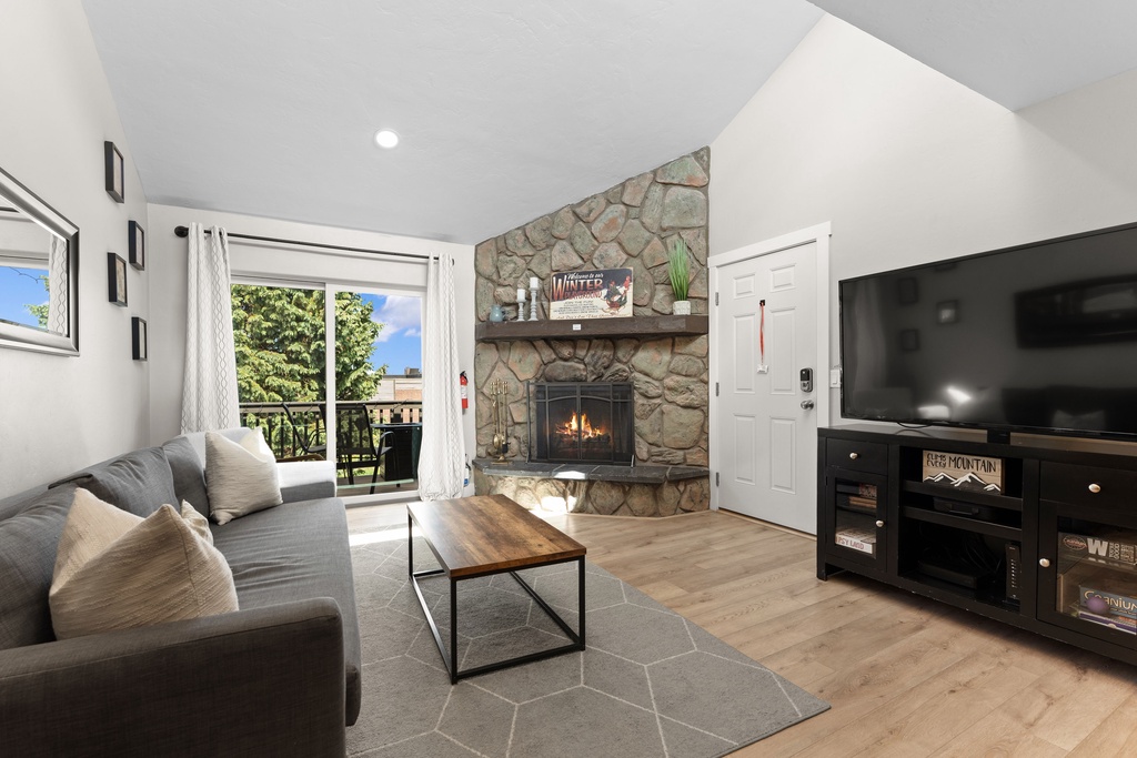 Unwind in your cozy living room with a stone fireplace, plush seating, and mountain views through the balcony doors—perfect for evenings of relaxation.