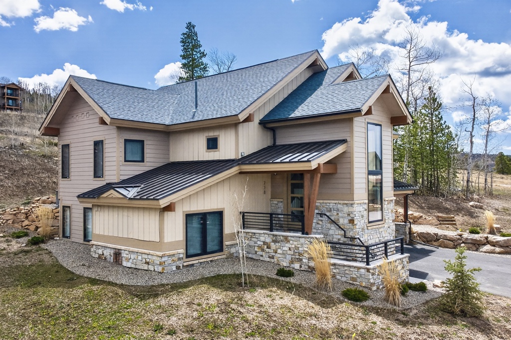 Modern mountain retreat featuring contemporary architecture with stone accents, metal roofing, and expansive windows set against a scenic hillside backdrop.