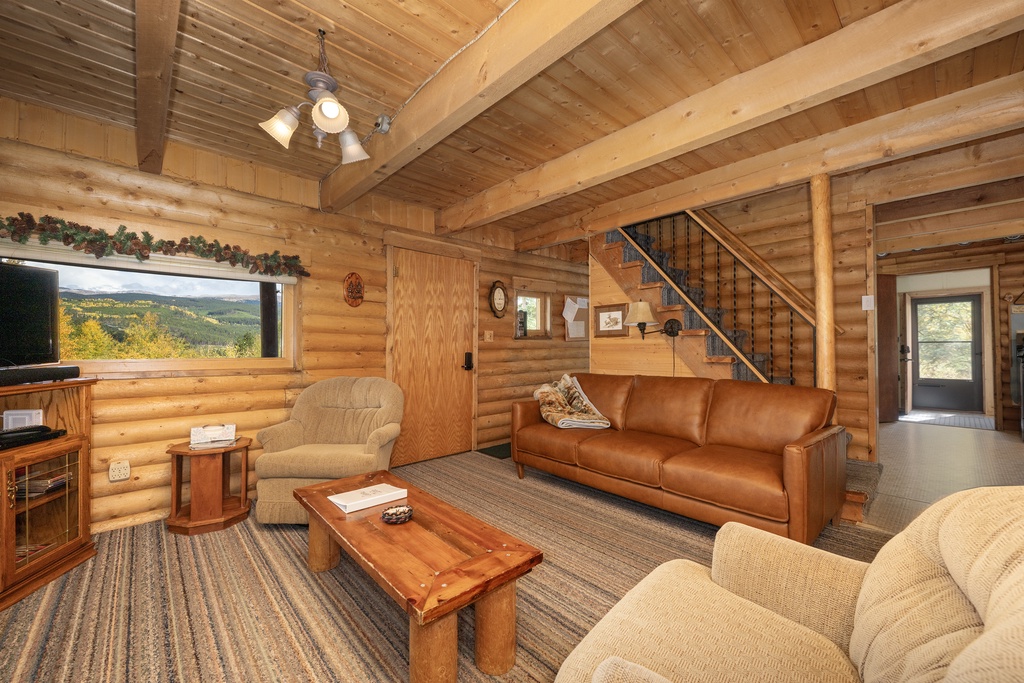 Unwind in this cozy log cabin living room, where exposed beams frame mountain views and comfortable seating invites you to relax.